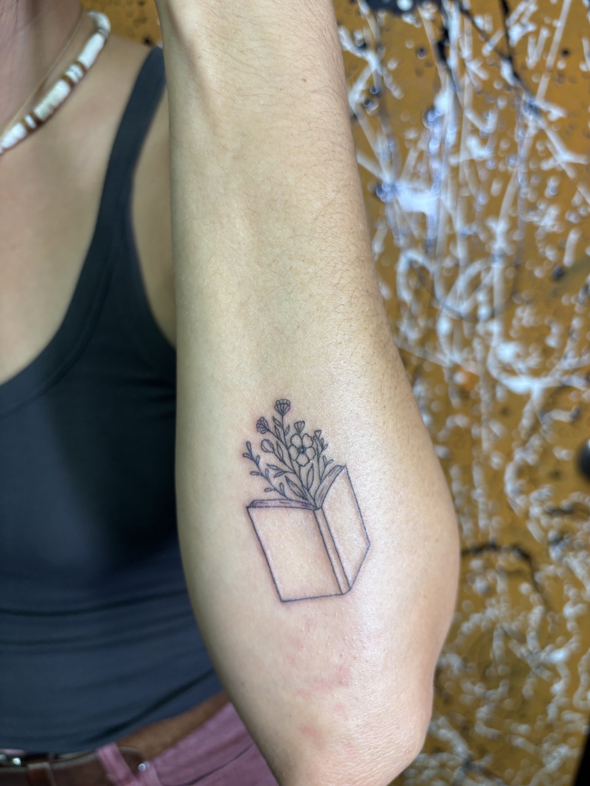 Fine line tattoo of an open book with flowers